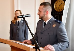 Oficer Policji przemawia na mównicy. W tle zastępca Naczelnika Wydziału Kadr i Szkolenia KWP w Białymstoku.