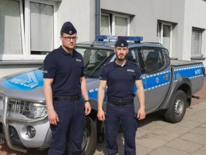 Zdjęcie w kolorze. Na pierwszym planie dwóch policjantów z Oddziału Prewencji Policji w Białymstoku. W tle radiowóz.