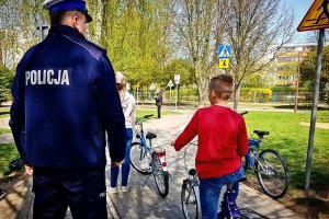 umundurowany policjant a obok siedzący na rowerze chłopiec w czerwonej bluzce