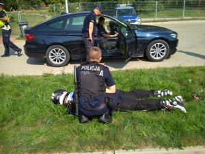 Policjanci zatrzymujący na trawniku motocyklistę. W tle nieoznakowany radiowóz BMW.