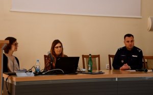 Zastępca Komendanta Wojewódzkiego Policji w Białymstoku przemawia siedząc wspólnie z dwiema prelegentkami.