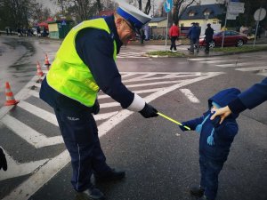 policjant ruchu drogowego w żółtej kamizelce, który przekazuje odblask dziecku