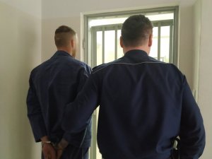 Policjant prowadzi do celi zatrzymanego mężczyznę.