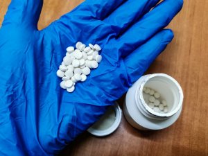 białe tabletki na niebieskiej rękawiczce obok mały pojemnik z tabletkami w środku