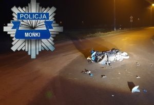 Gwiazda policyjna z napisem Policja Mońki. Na drodze leży uszkodzony skuter. W tle pora nocna.