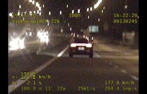 Jest już zmrok. Pojazd z włączonymi światłami jedzie lewym pasem i wyprzedza pojazdy jadące prawym pasem. Na zdjęciu są cyfry wyświetlone z videorejestratora.
