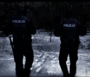 Policjanci idą po śniegu w lesie