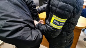 policjant w ubraniach cywilnych zakłada zatrzymanemu kajdanki na ręce trzymane z tyłu