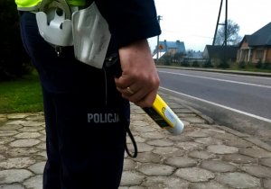 Policjant stoi przy drodze, trzyma alkomat.