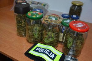 słoiki z narkotykami na stole przed nimi odblaskowy emblemat z napisem policja