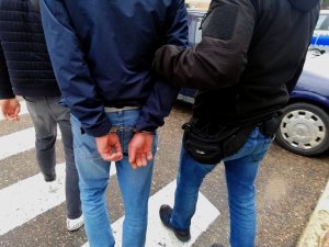 policjanci prowadzą zatrzymanego mężczyznę, który ma założone kajdanki na ręce trzymane z tyłu