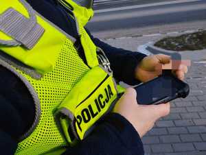 Policjant ruchu drogowego trzyma w dłoni urządzenie do sprawdzania w policyjnej bazie danych